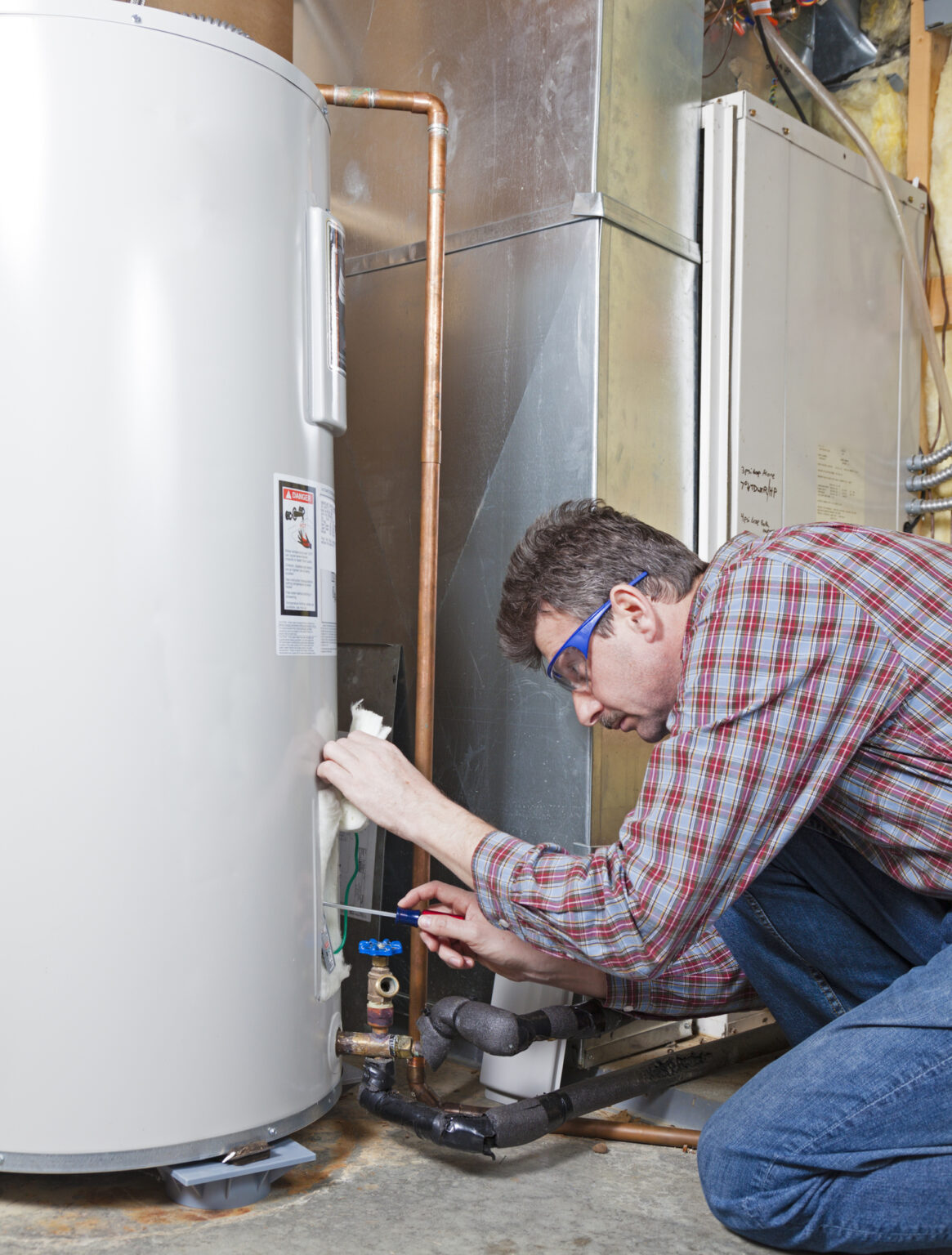 A man in a flannel fixing the bottom part of a water heater with a screwdriver