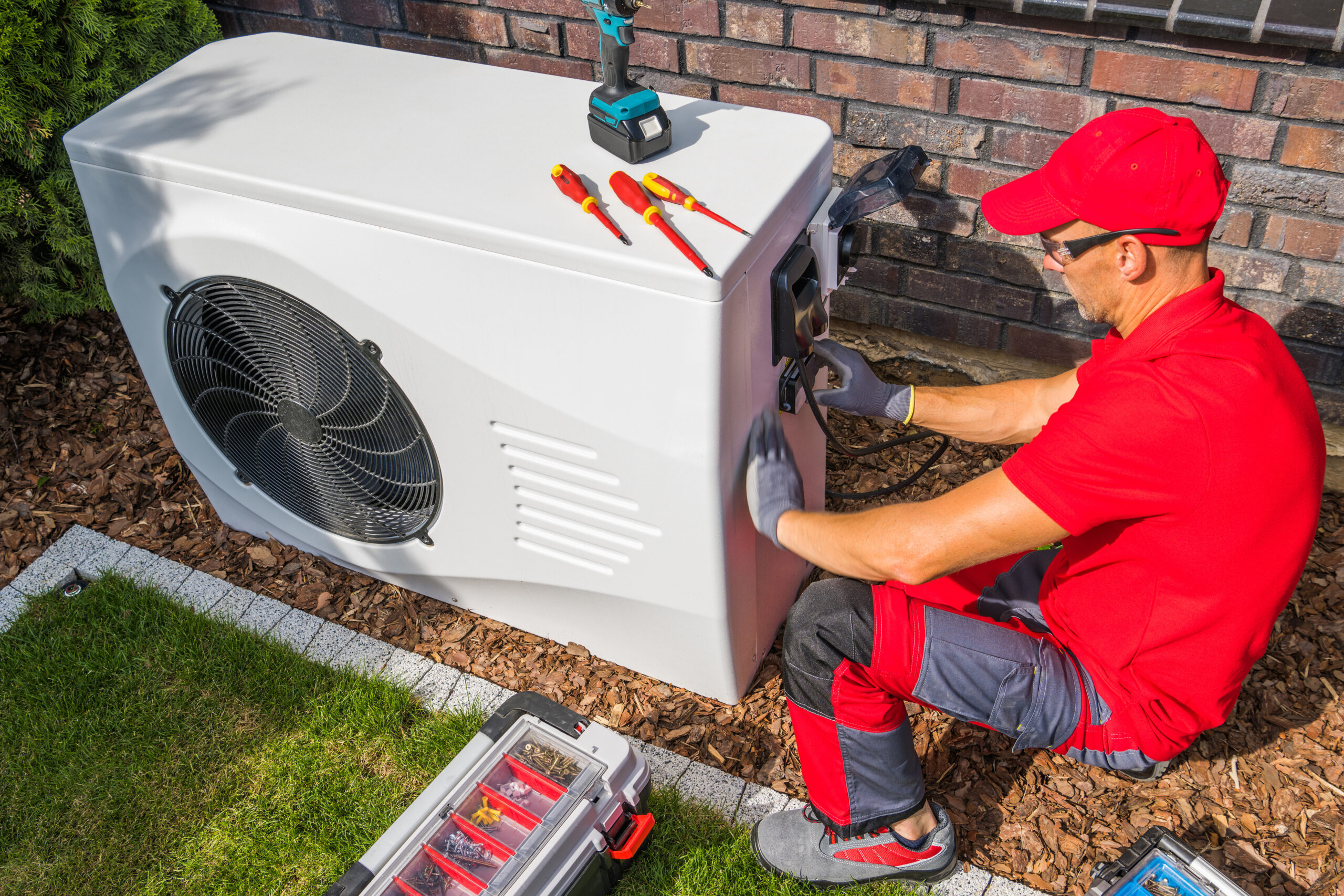 Professional HVAC technician in red uniform performing a tune-up of modern heat pump unit 