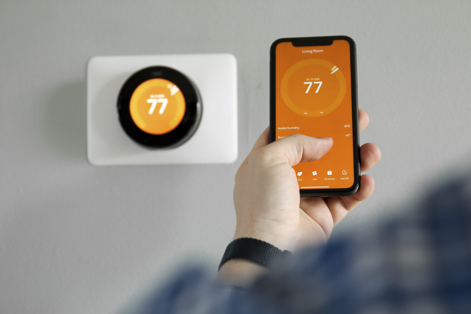 Man uses a mobile phone with smart home app to adjust temperature in home