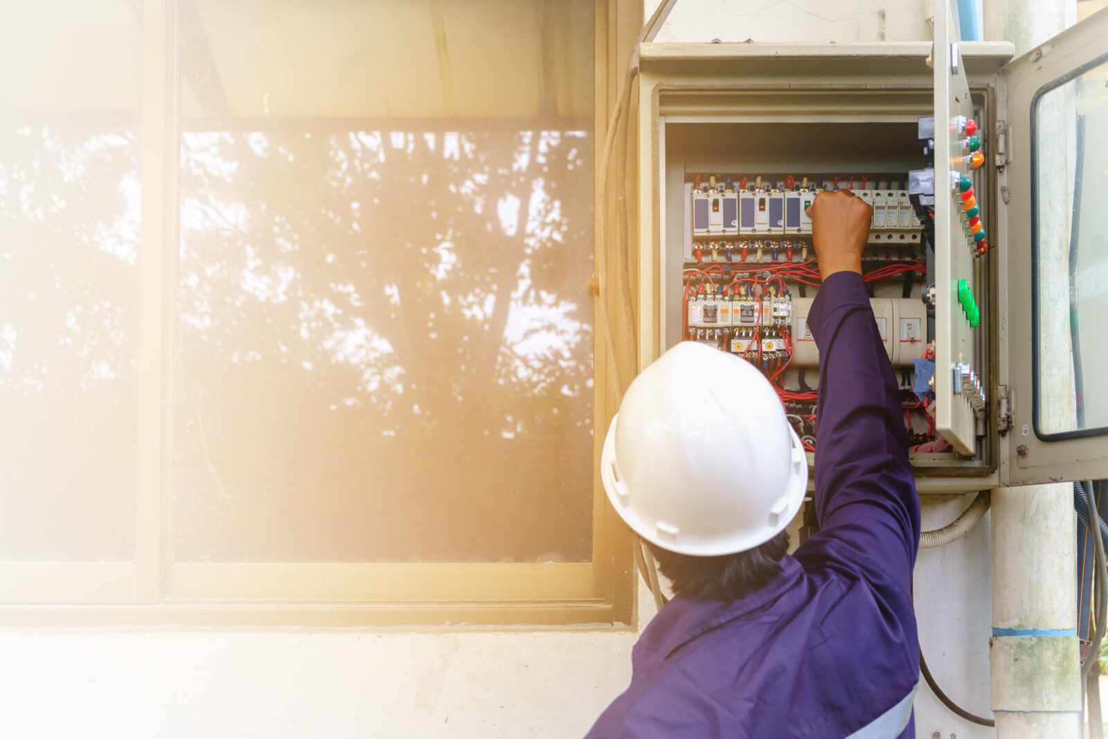 technician in safety uniform and white security helmet turning on switch in the electrical cabinet