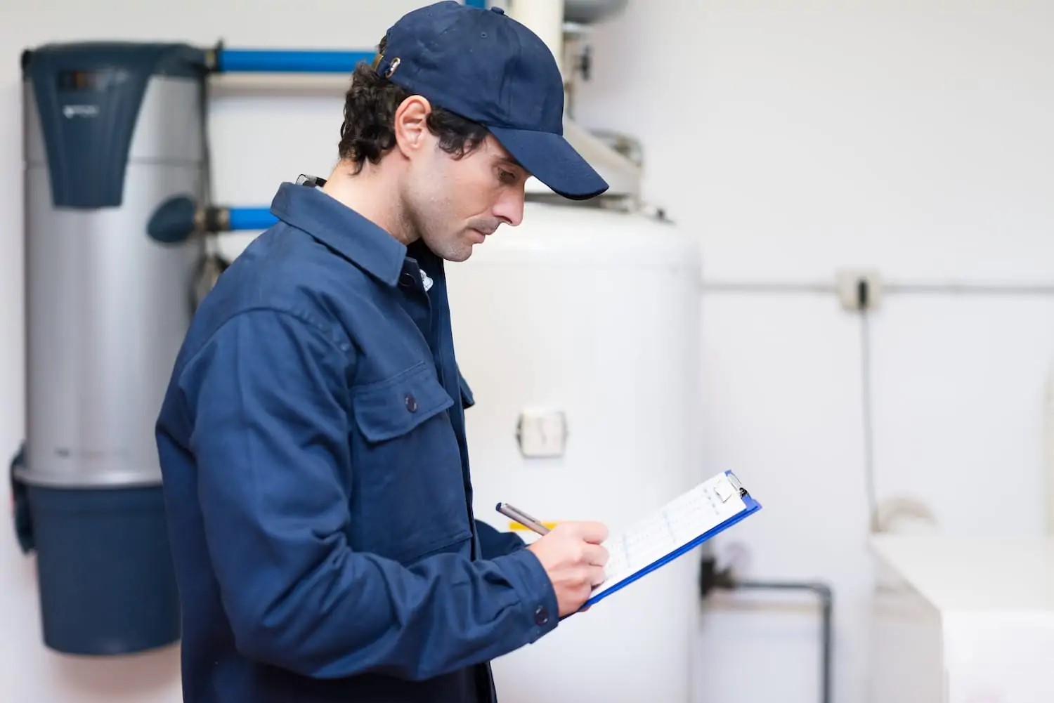 Plumber standing in front of a tanked & tankless water heater with a clipboard